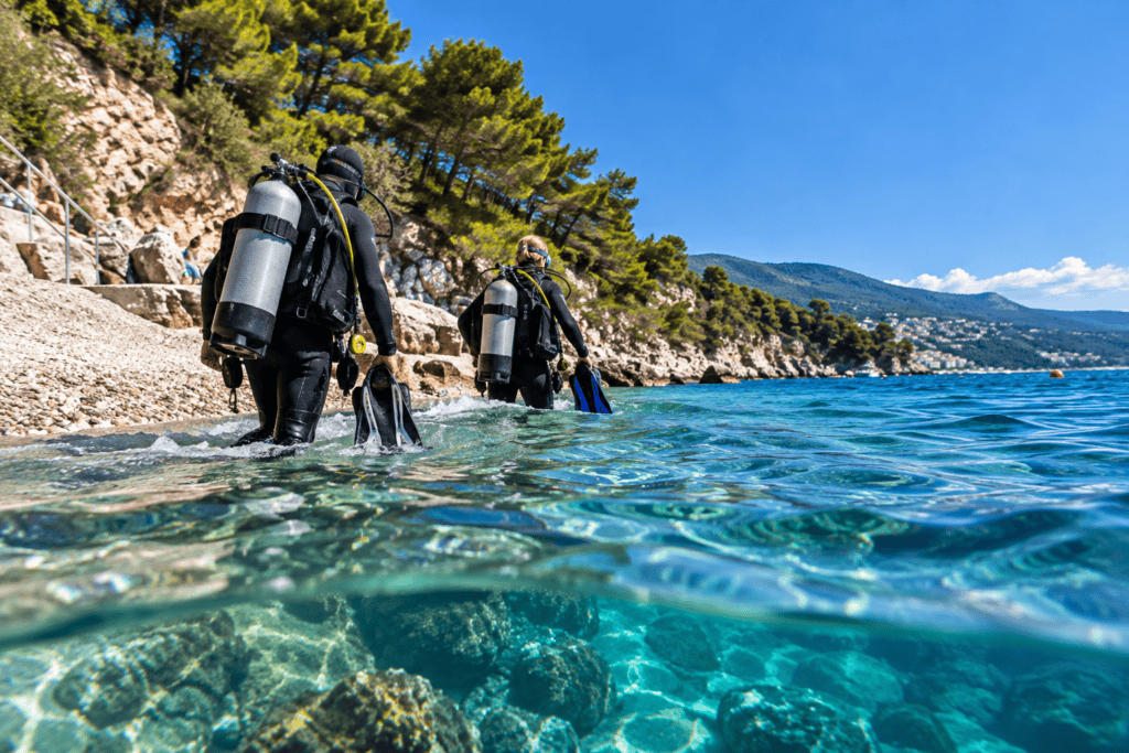 Tauchgänge in Rabac am Hausriff Girandella: Zwei Taucher steigen ins türkisfarbene Meer ein.